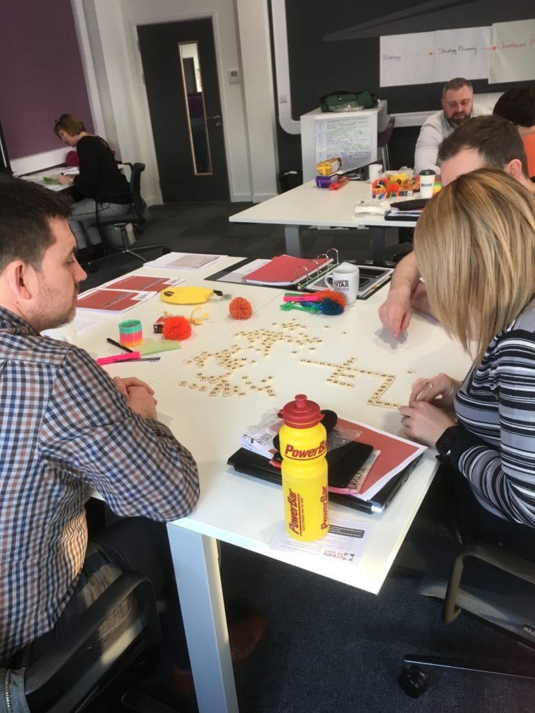 A group of two men and one woman take part in a learning exercise using Scrabble pieces as part of a talent development programme.