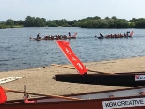 Two of the dragon boats on the shore, with two other dragon boats racing in the water in the background.